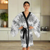 Woman wearing a chic long sleeve kimono robe with black and white tropical floral print and black trim, tied at the waist, standing in a modern kitchen.